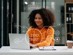 A professional woman works on her laptop in a modern office, with a digital overlay reading “Zero Trust.” The image represents secure, identity-based remote access and the shift from traditional VPNs to Zero Trust Network Access.
