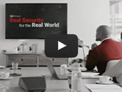 Real Security for the Real World displayed on a wall-mounted tv while a man in a red sweater watches