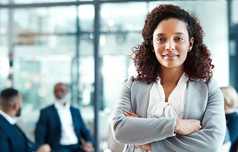 Woman in a gray blazer standing in an office with her arms crossed